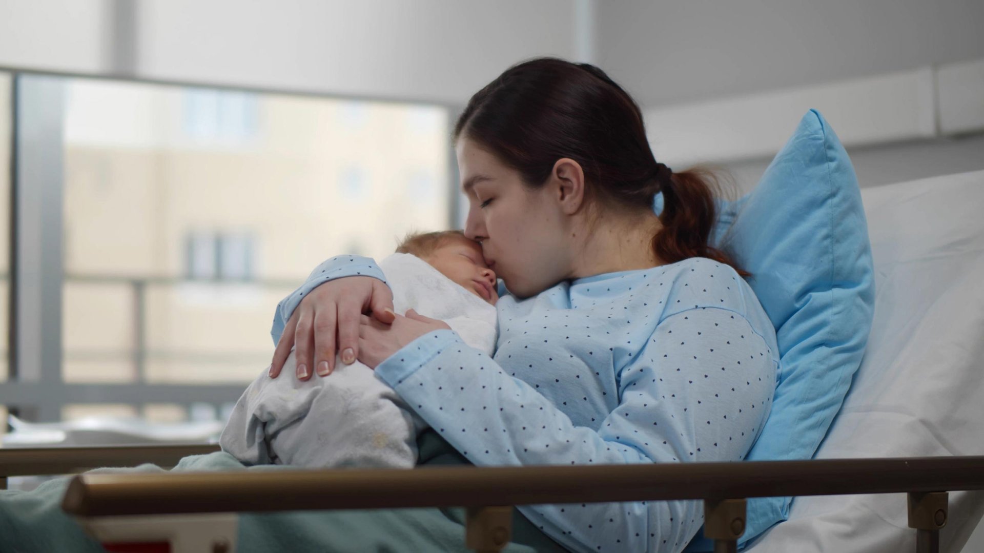Kobieta caluje w czolo noworodka po porodzie