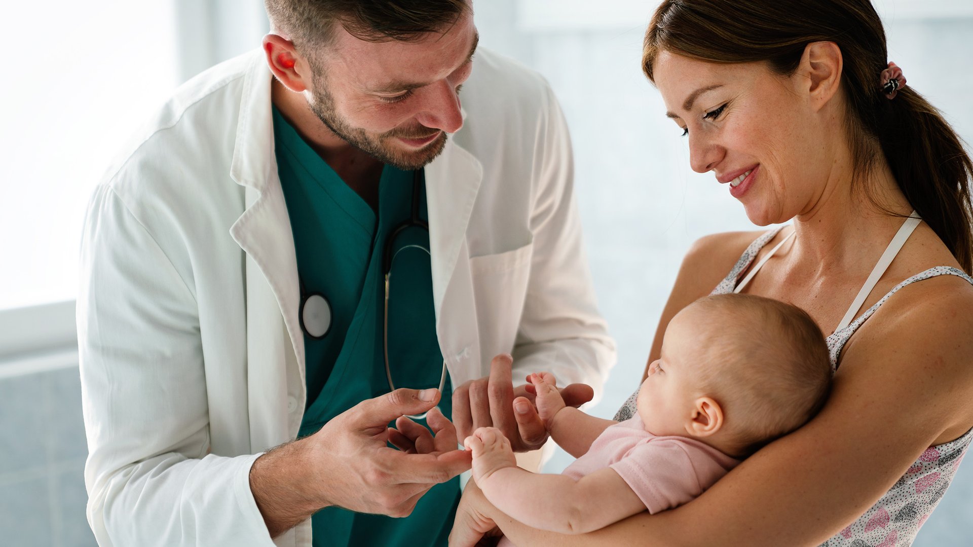 Lekarz trzyma za raczki dziecko siedzace na rekach mamy