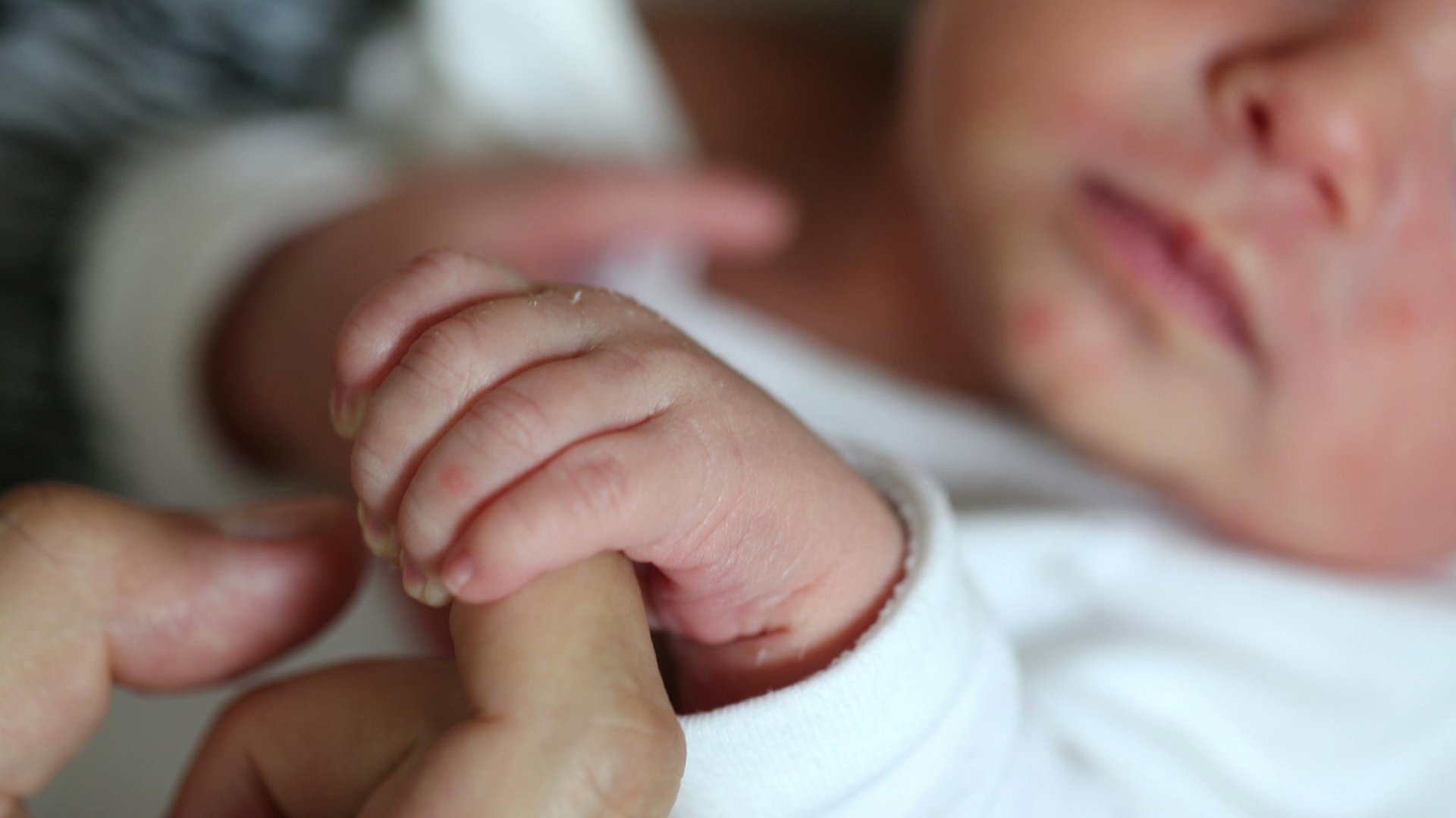 Noworodek trzyma reka rodzica za palec