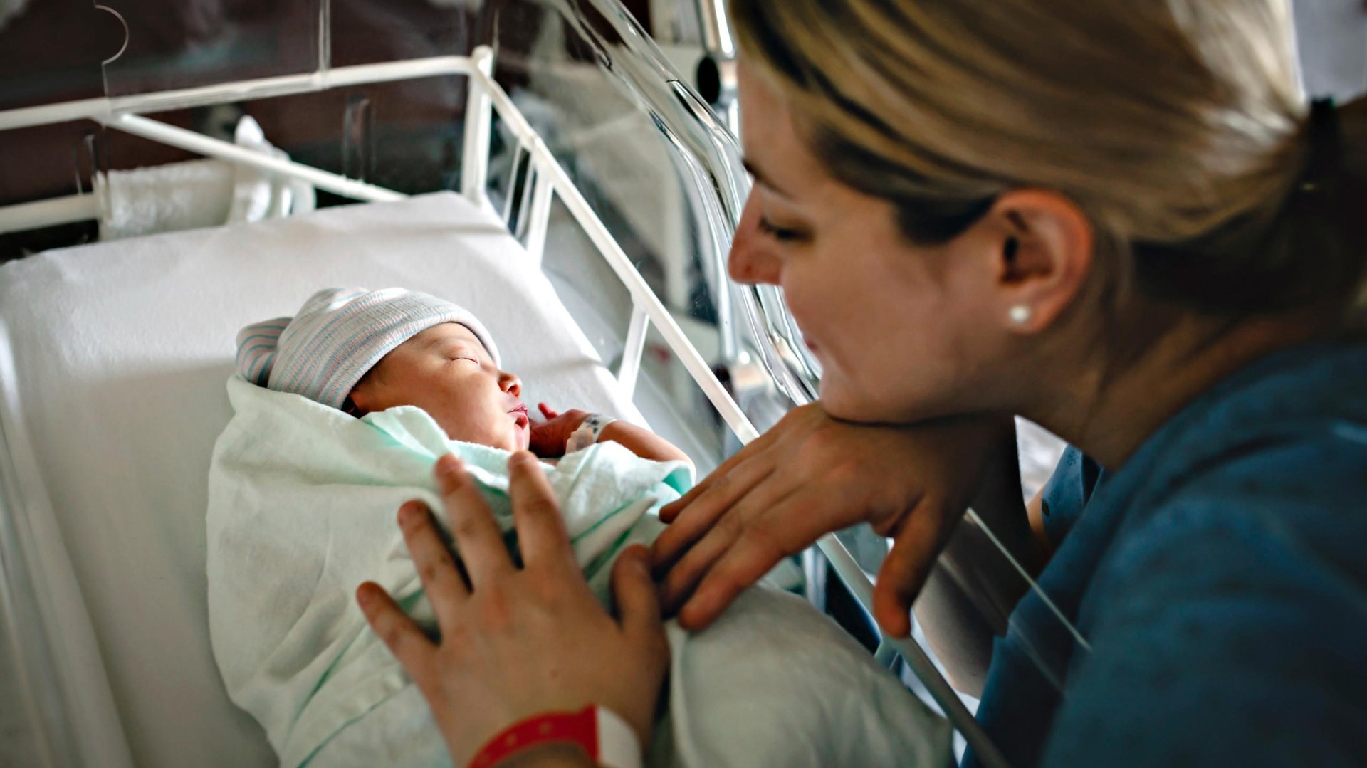 Mama przyglada sie noworodkowi lezacemu w lozeczku