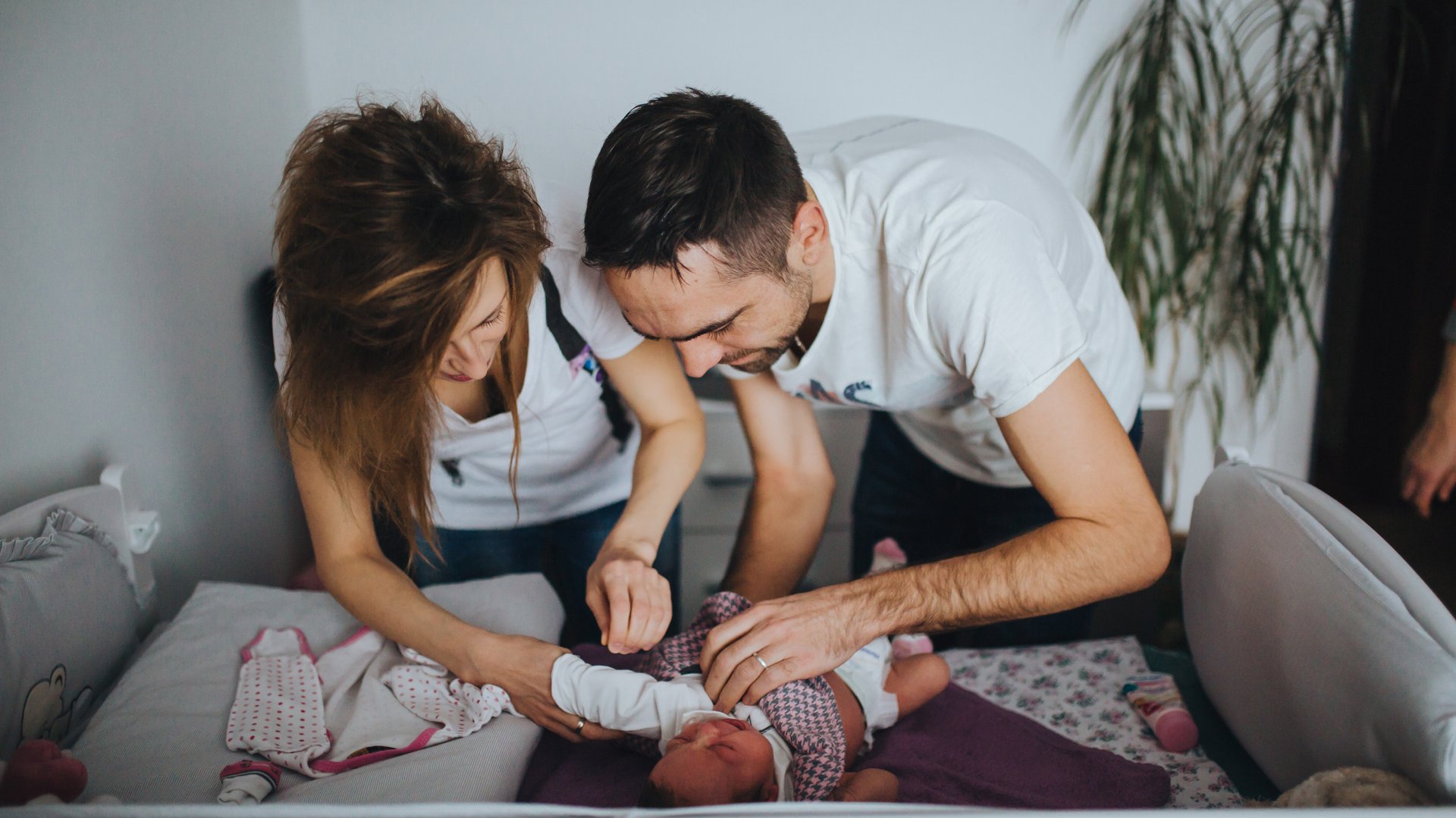 Rodzice pochylaja sie nad dzieckiem ubierajac je