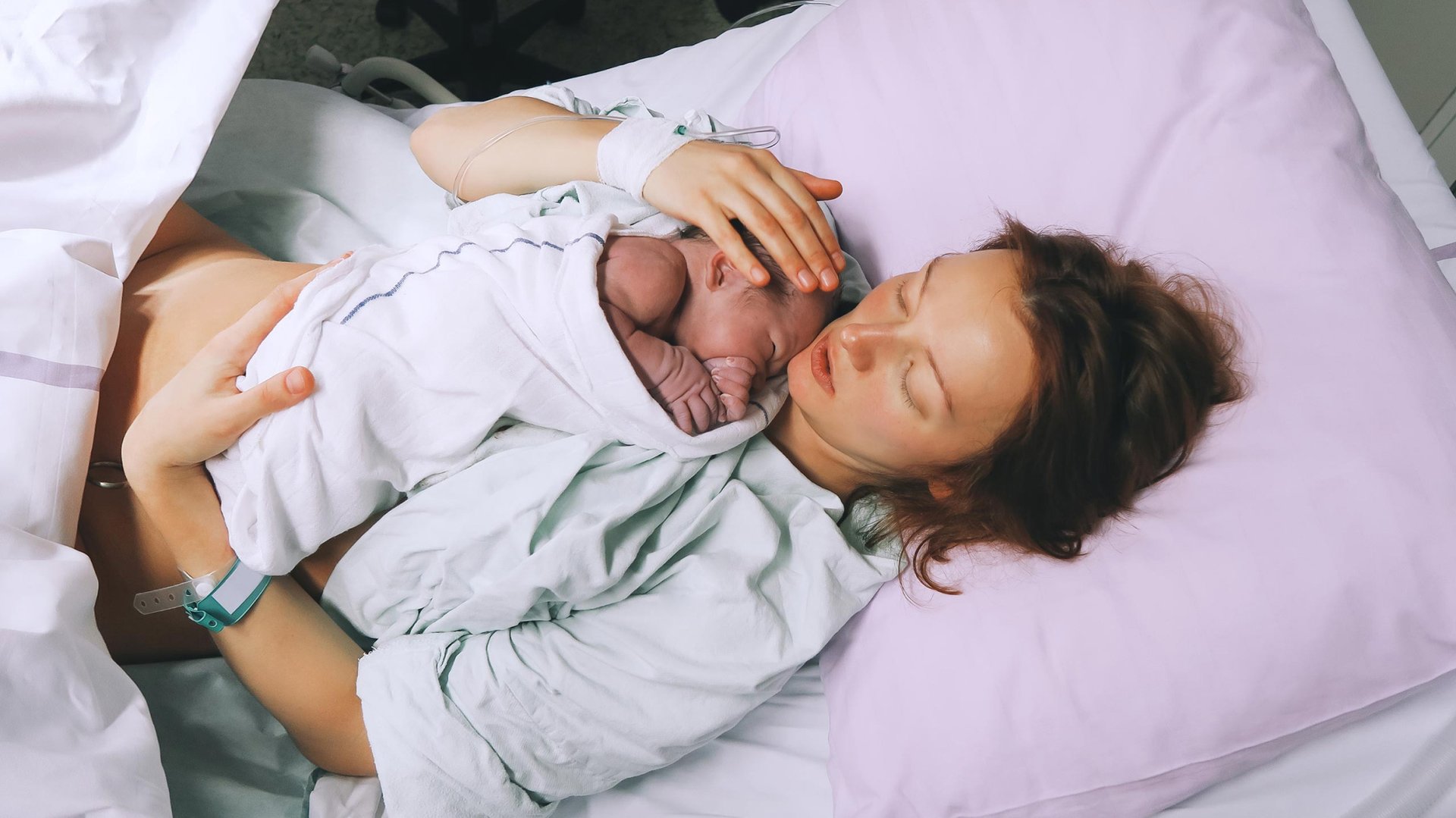 Mama lezy w lozku szpitalnym z dzieckiem po porodzie