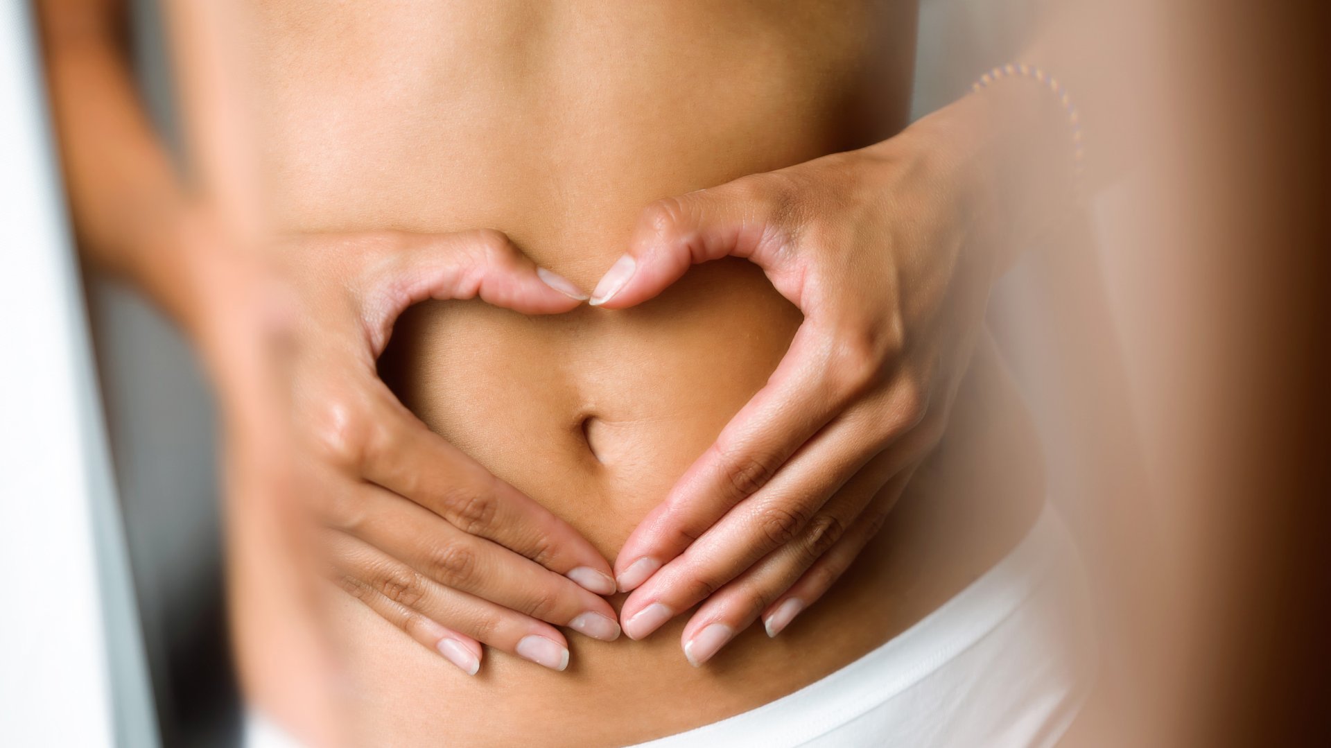 Kobieta z płaskim brzuchem trzyma rece zlozone w serce