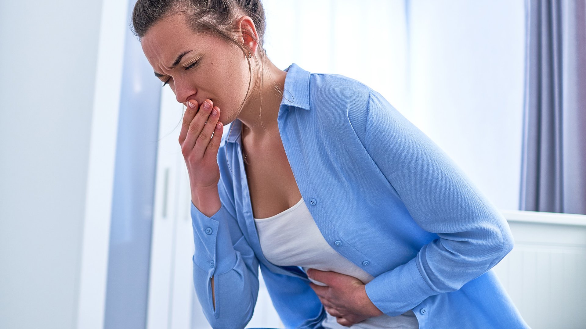 Kobieta trzyma reke na ustach majac nudnosci