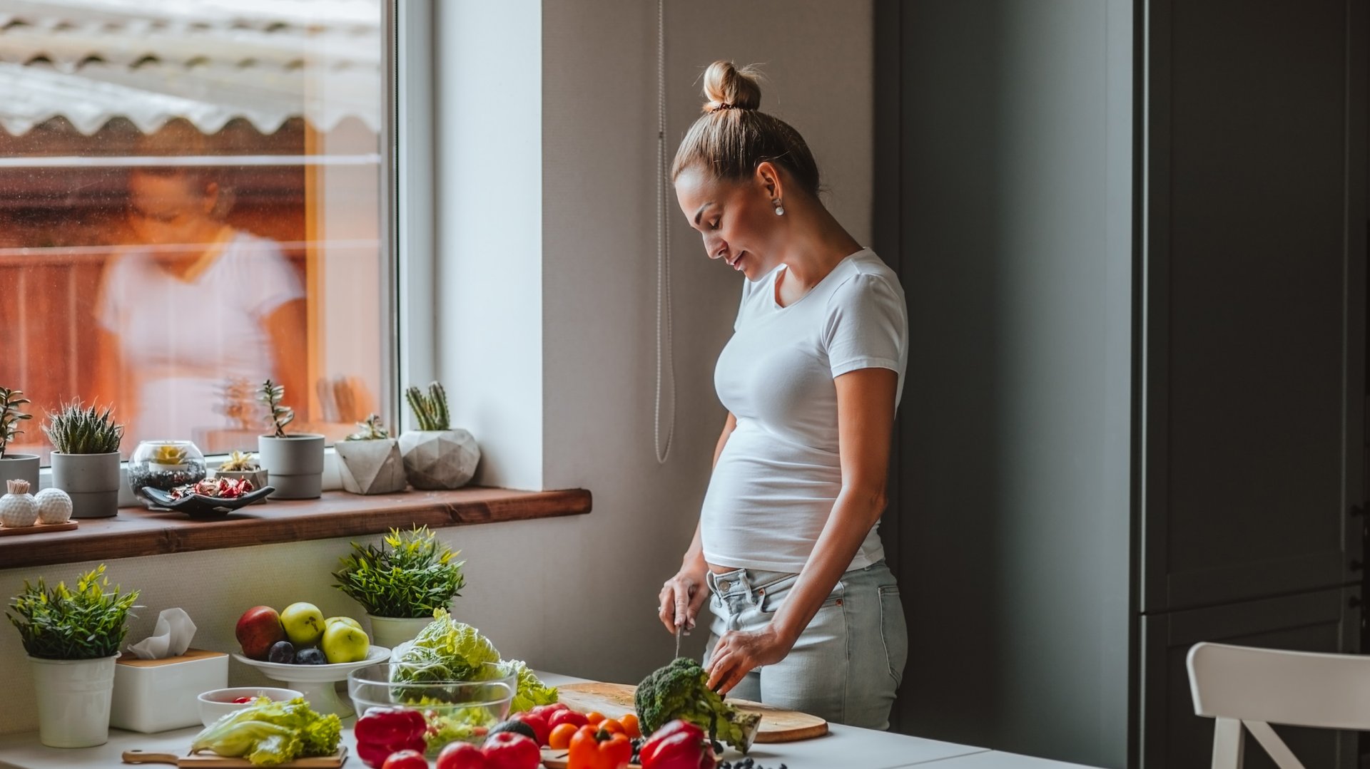 Kobieta w ciazy kroi warzywa na desce stojac w kuchni