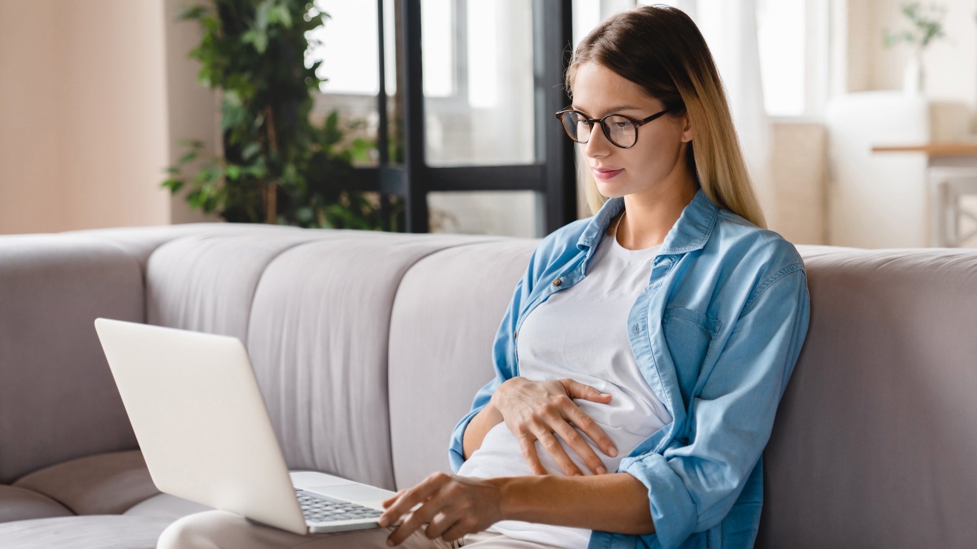 Kobieta w ciazy siedzi na kanapie z komuterem na kolanach