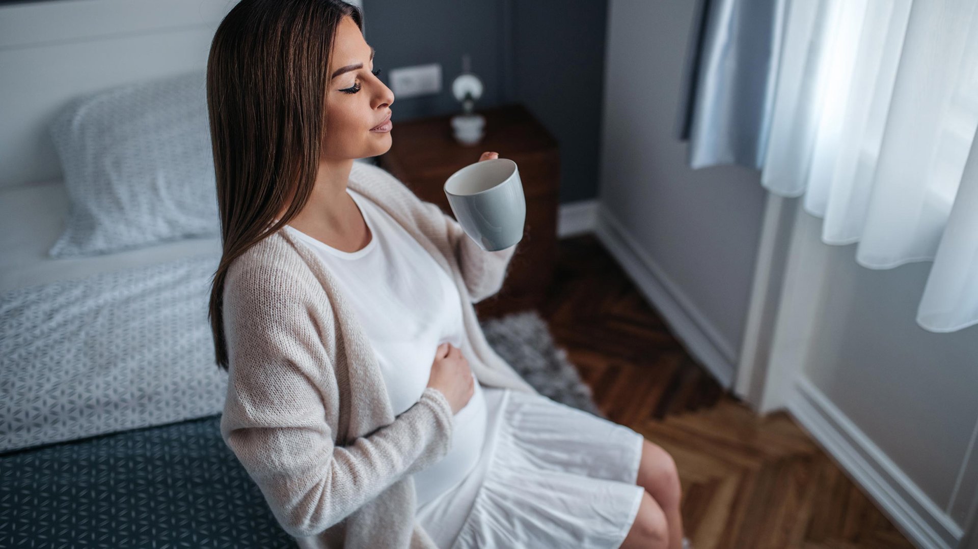 Kobieta w ciazy pije herbate trzymajac sie za brzuch