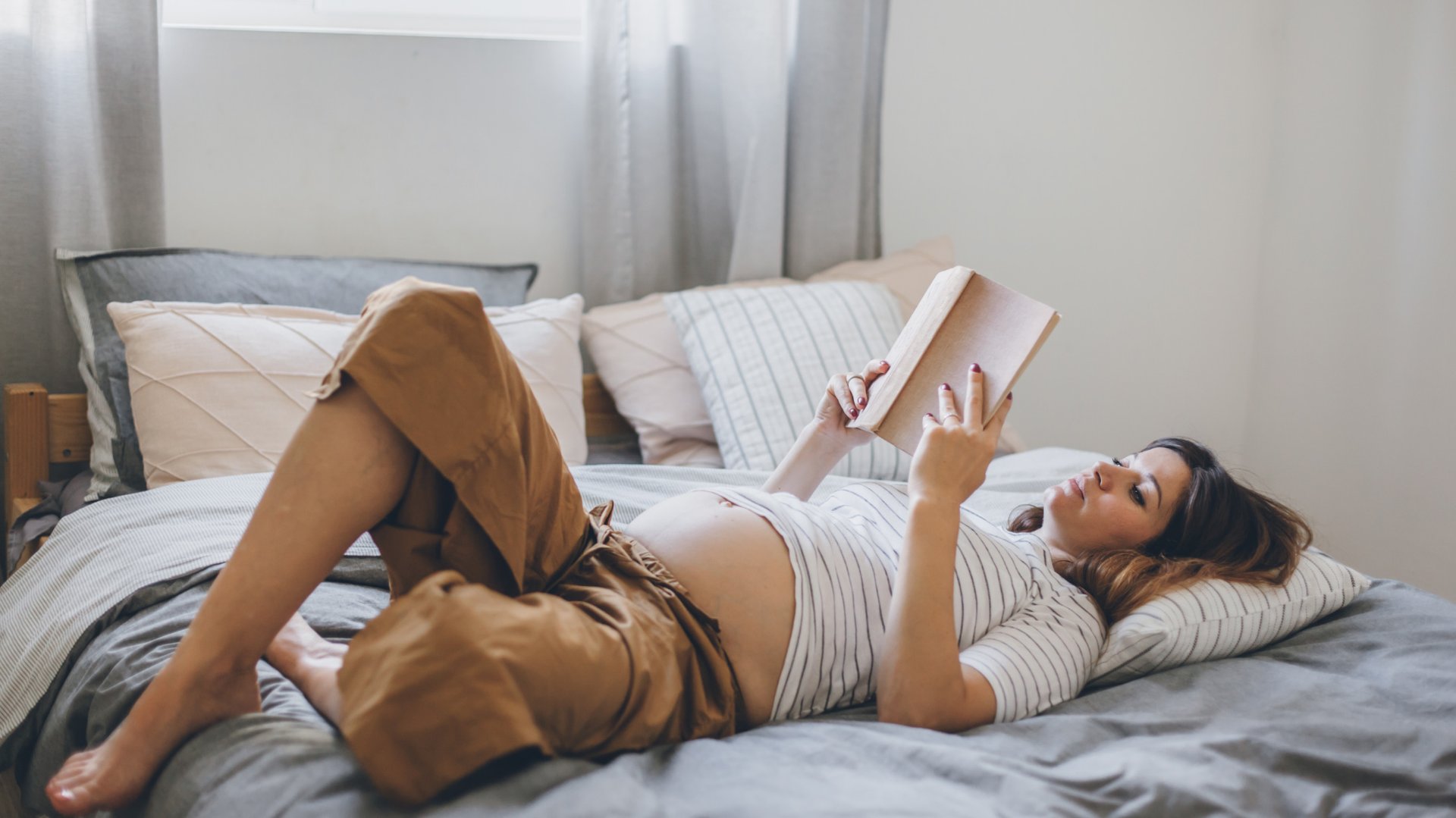 Kobieta w ciazy lezy na lozku czytajac ksiazke