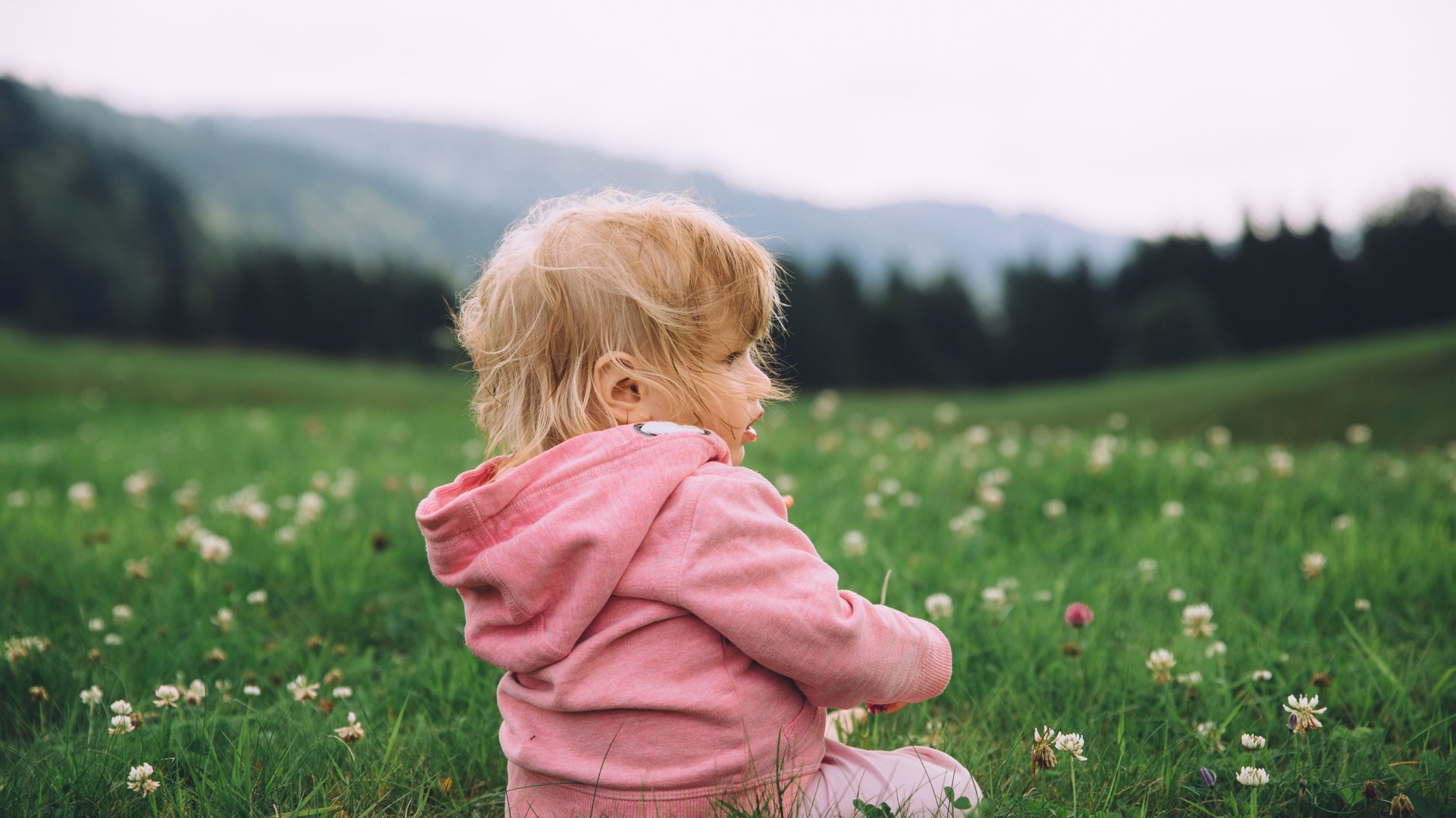 Dziewczynka w rozowym dresie siedzi na polanie