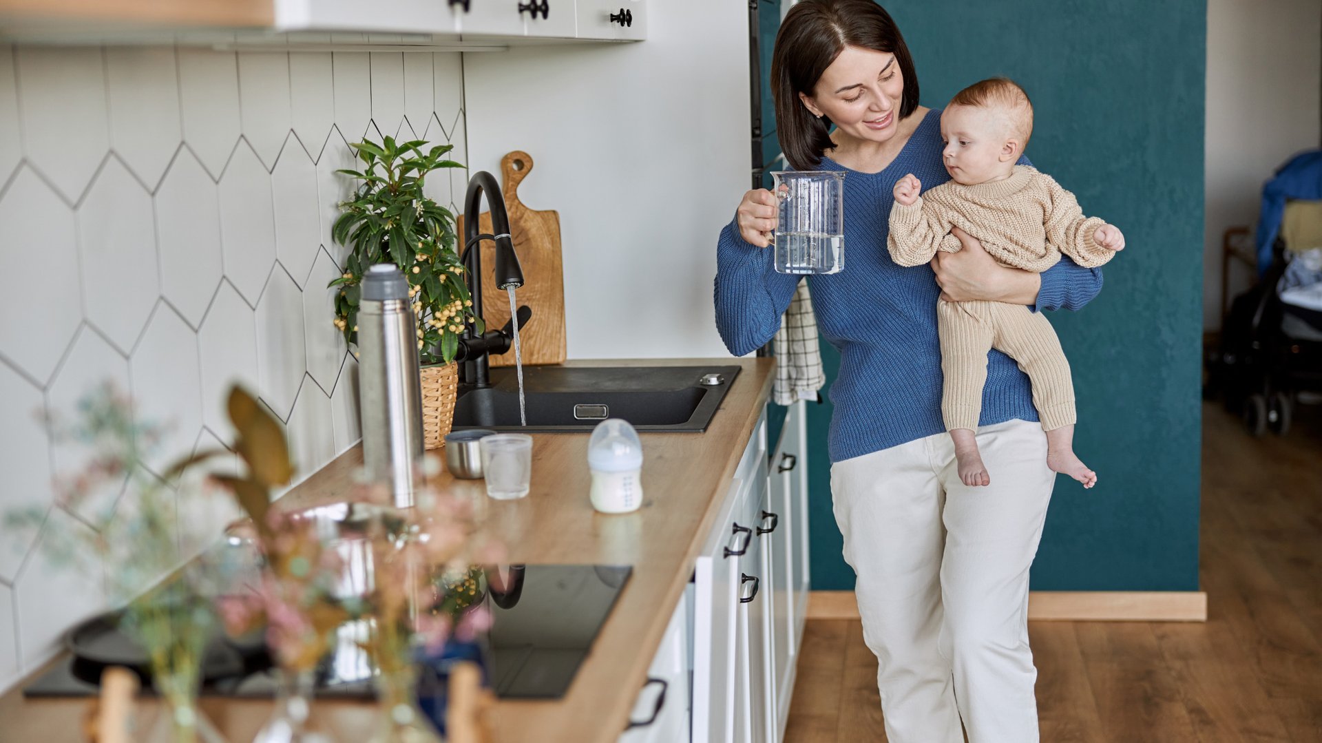 Kobieta nalewa wode do szklanki stojac w kuchni z dzieckiem