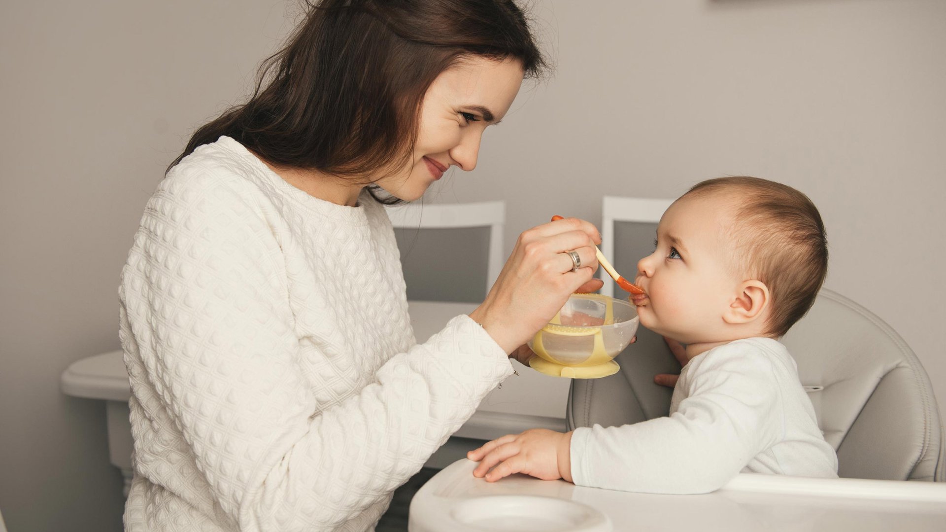 Mama karmi dziecko lyzeczka jedzeniem z miski