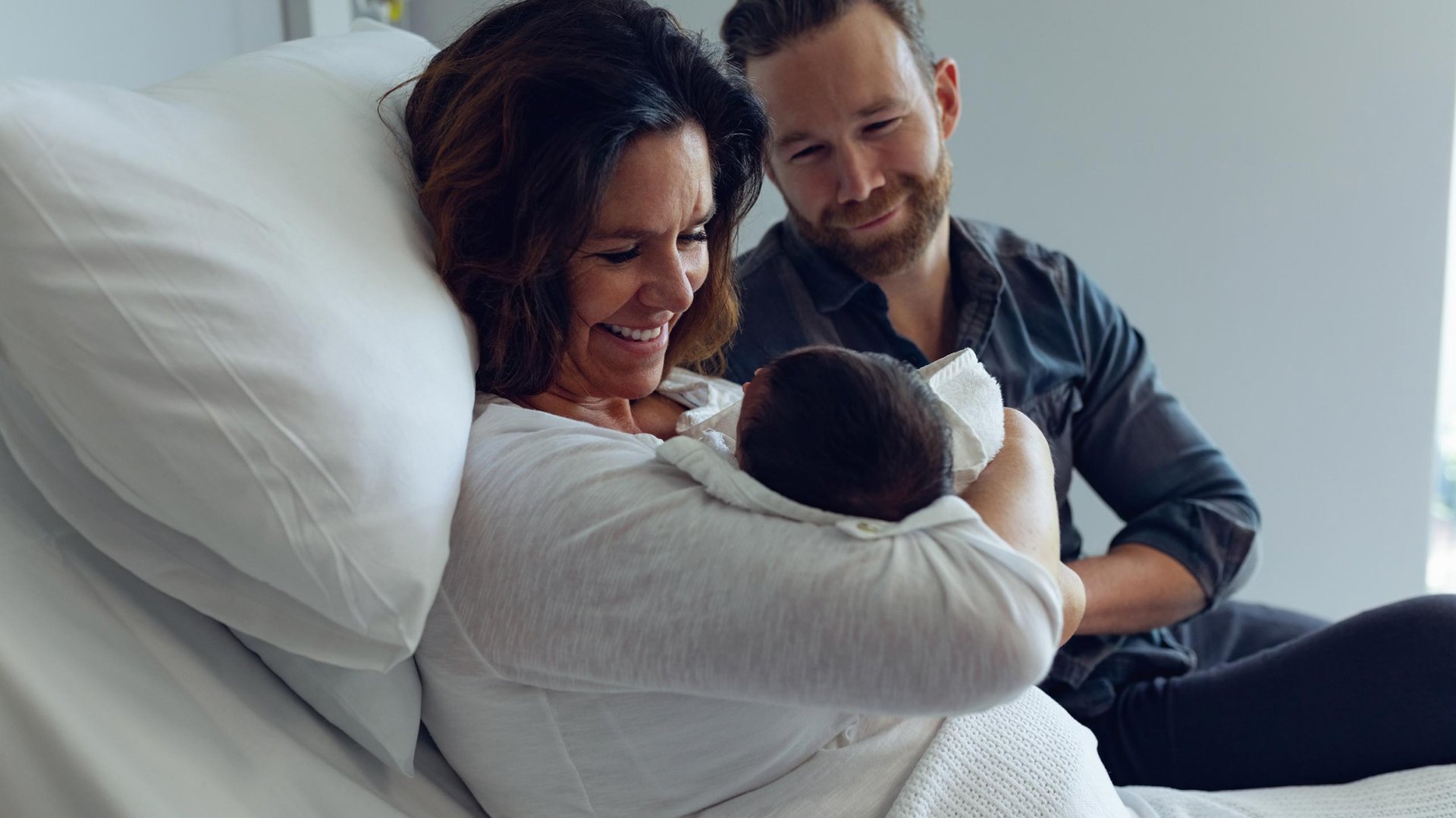 Rodzice podziwiaja noworodka siedzac na szpitalnym lozku