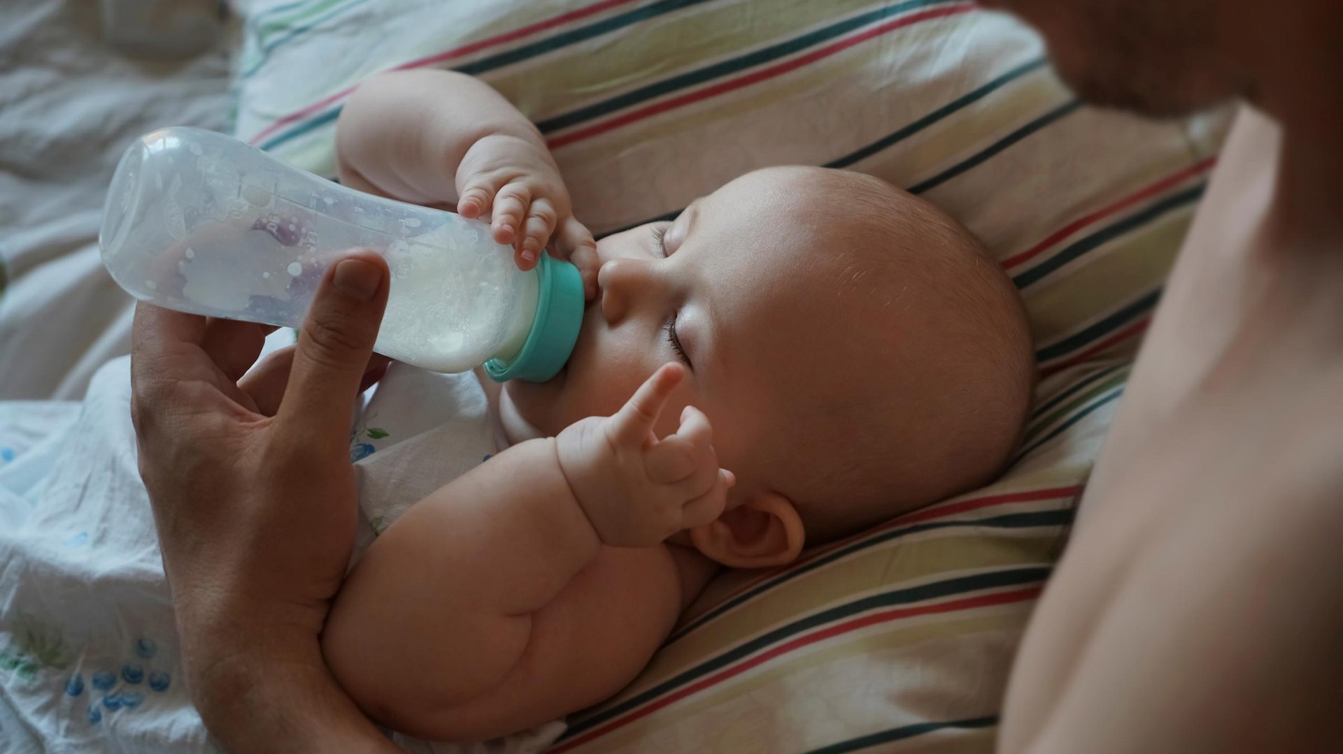 Mama karmi dziecko lezace na poduszce mlekiem z butelki