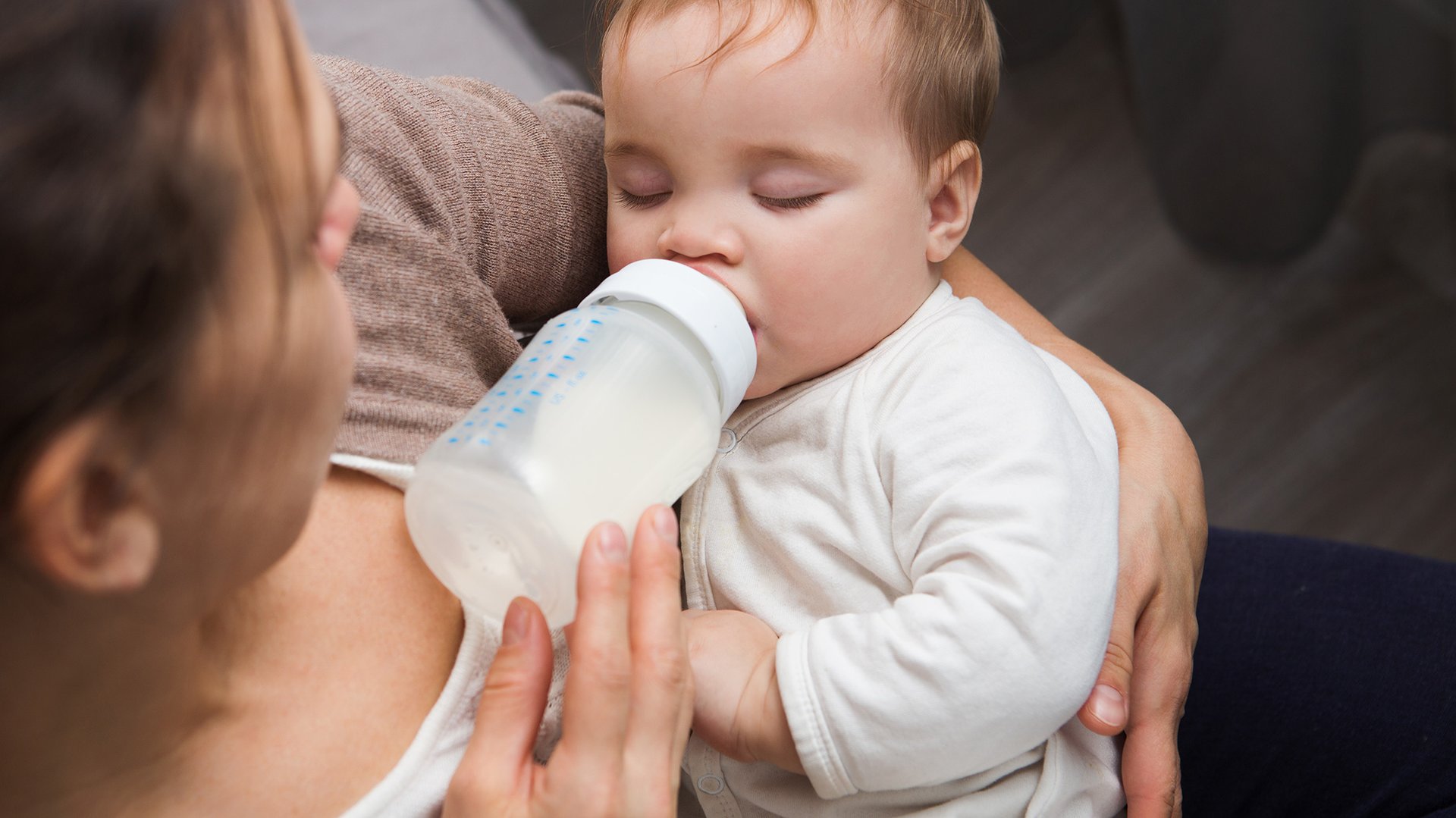 Dziecko z zamknietymi oczami pije mleko z butelki