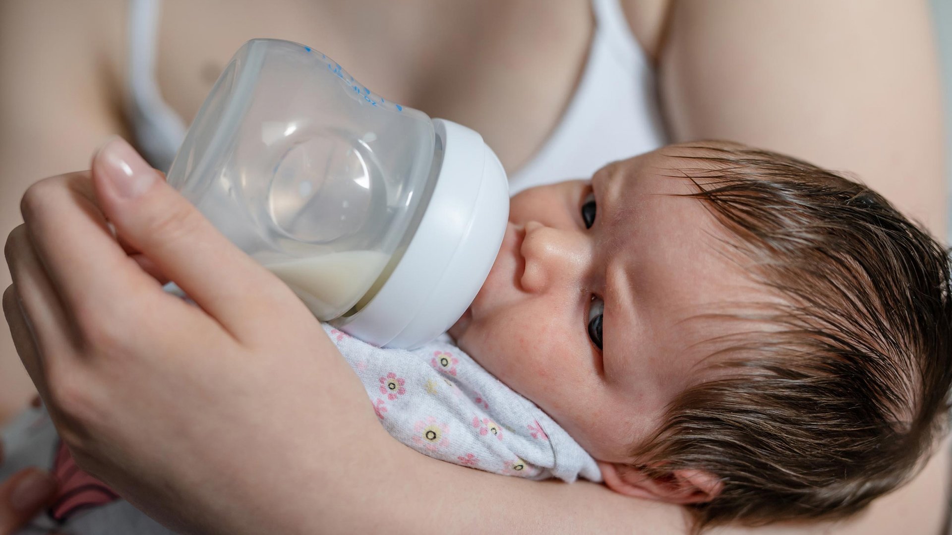 Dziecko pije mleko z butelki lezac na ramionach mamy
