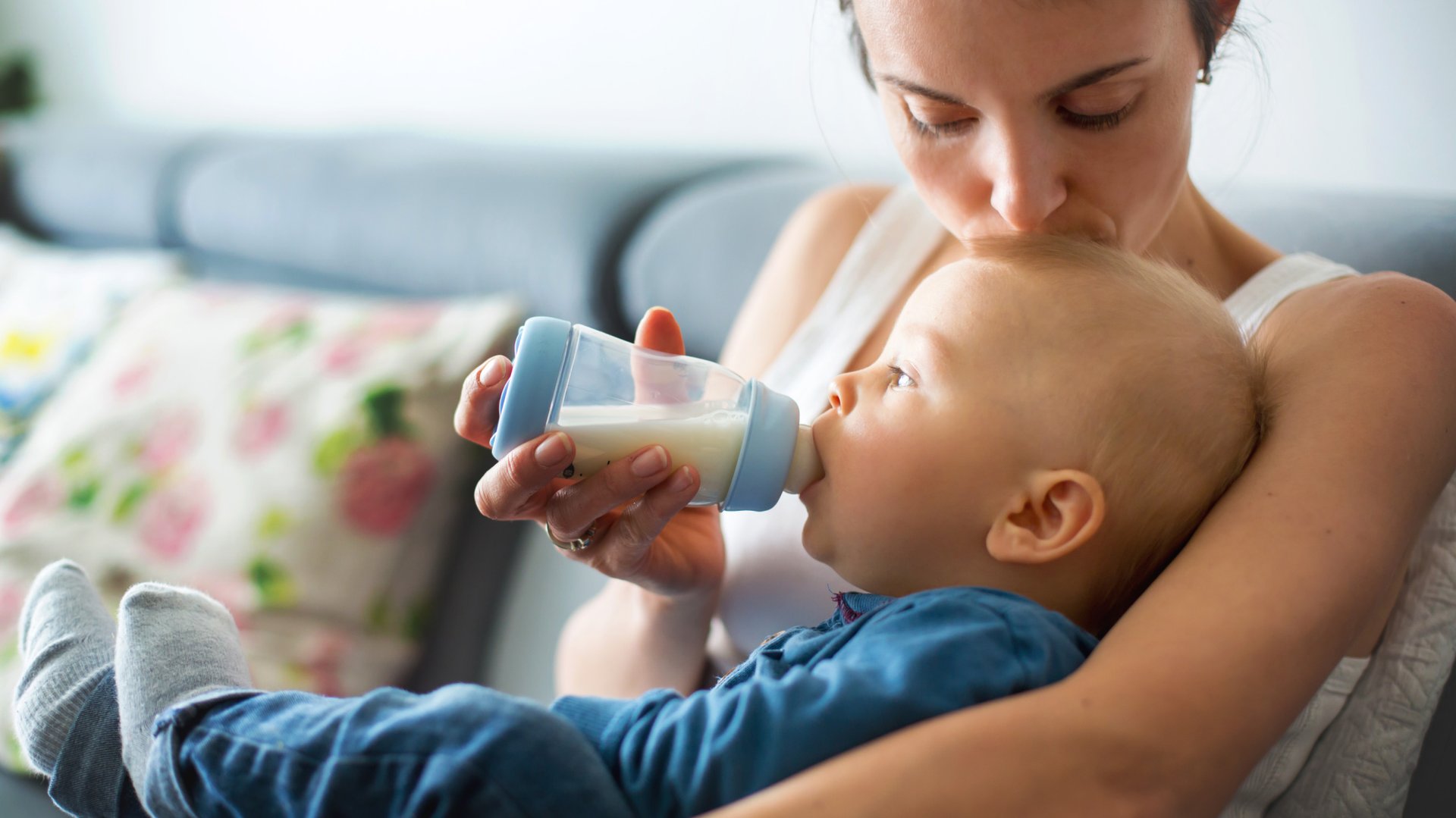Mama caluje dziecko w czolo karmiac je mlekiem z butelki