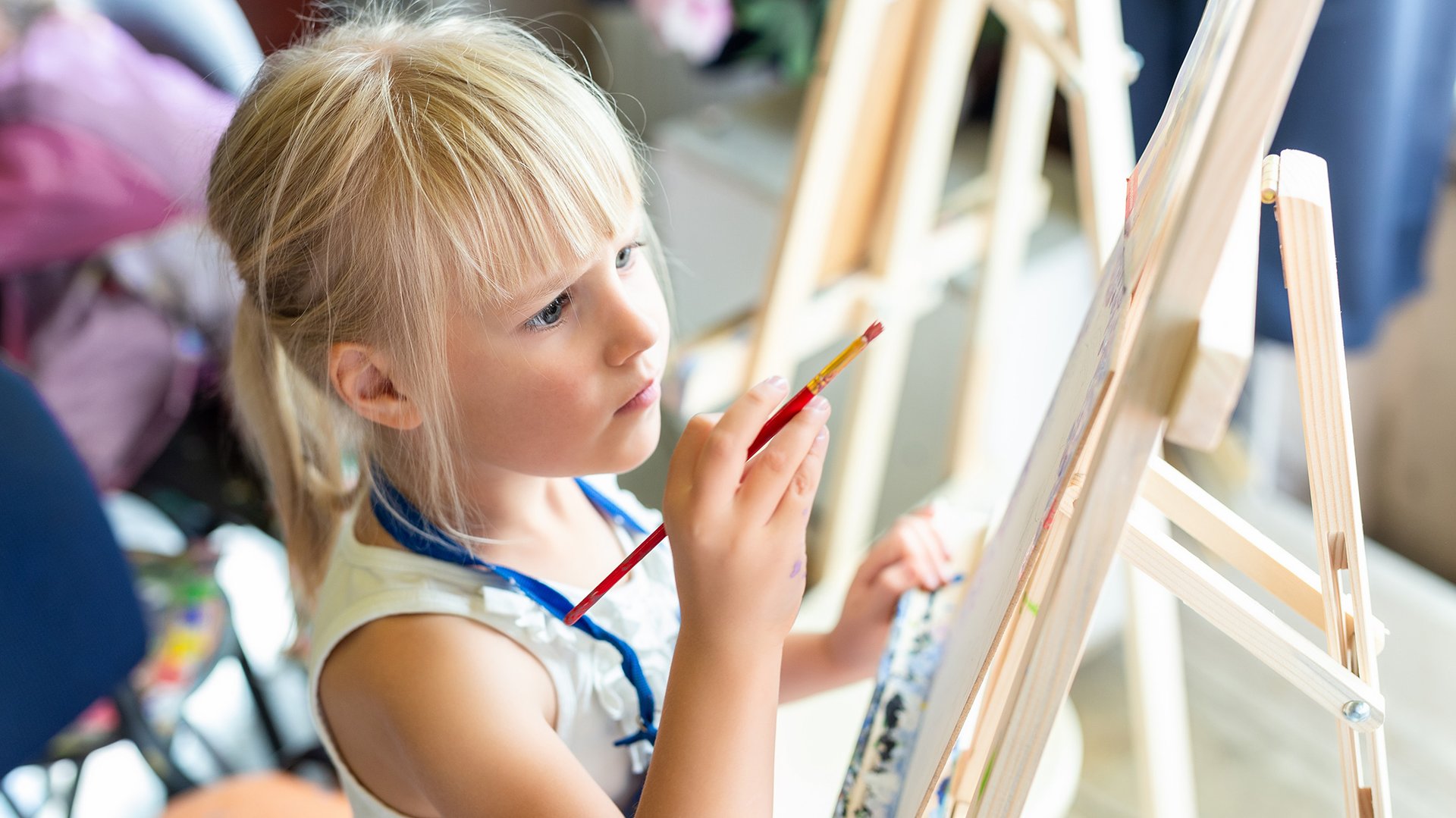 Dziewczynka maluje pedzlem obraz na sztaludze