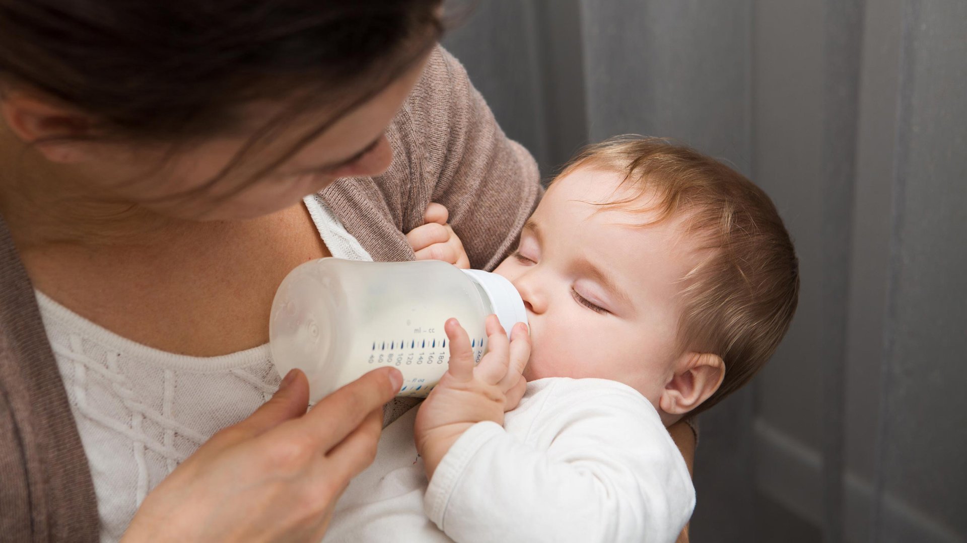 Dziecko trzyma podawna przez mame butelke z mlekiem
