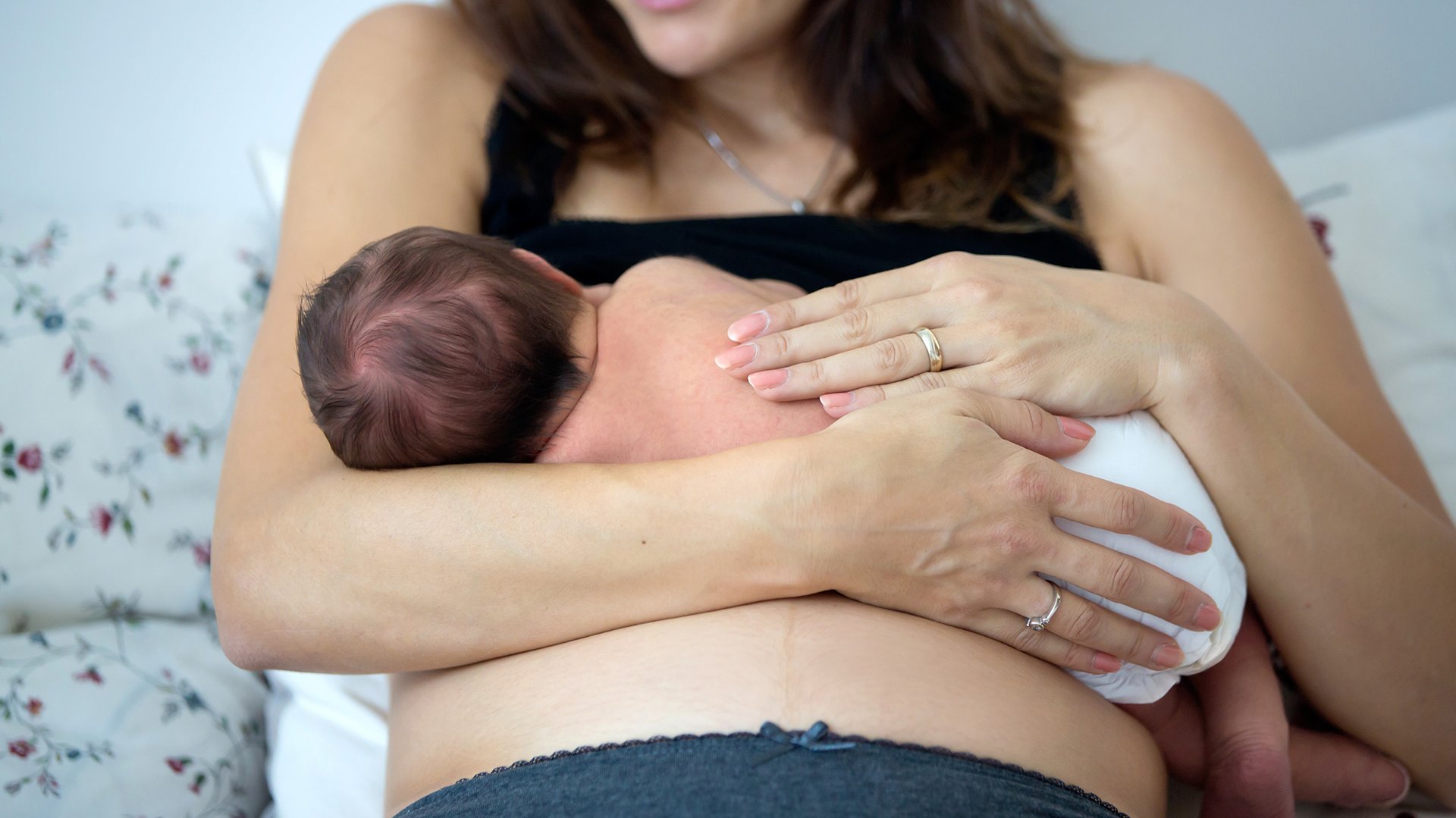 Kobieta karmi piersia niemowlaka trzymajac do na brzuchu
