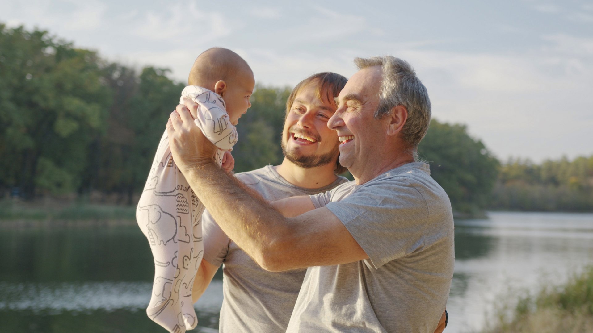 Dziadek podnosi dziecko do gory usmiechajac się wraz z tata